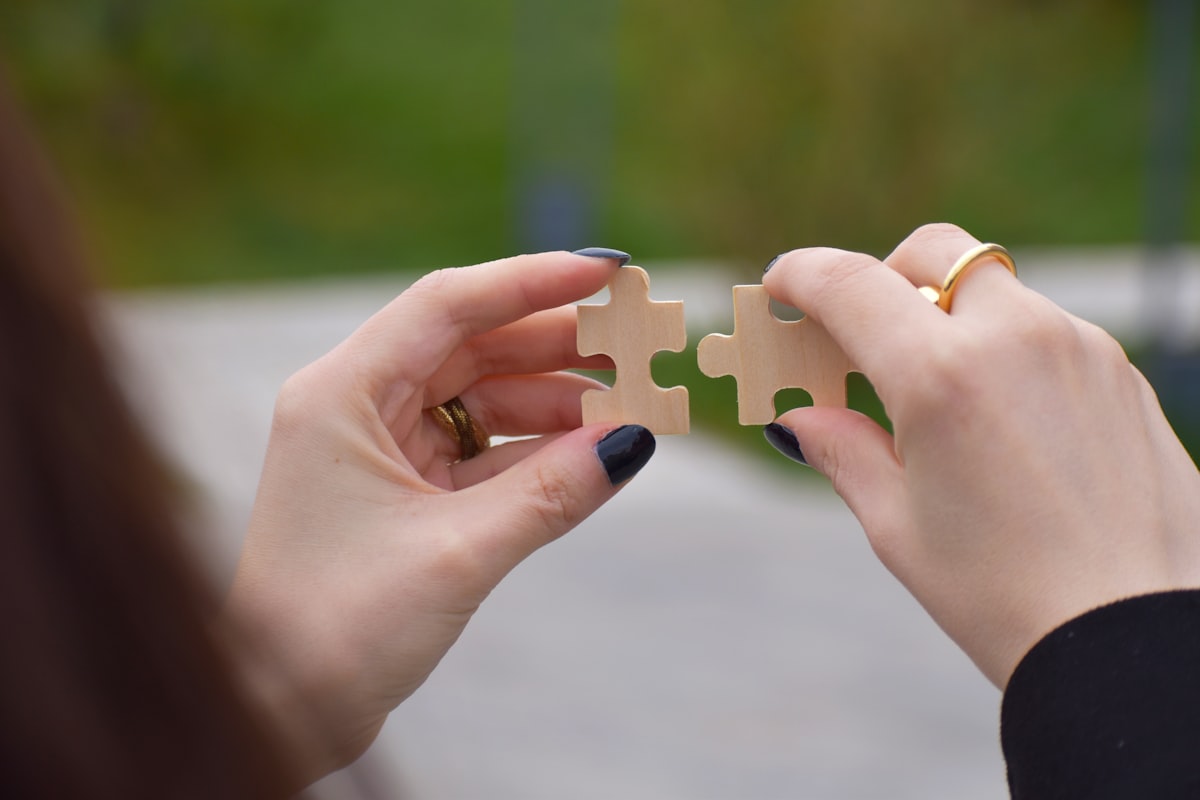 Zwei Hände fügen Holzpuzzleteile zusammen